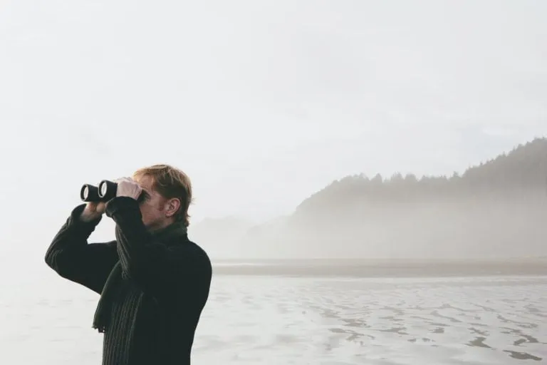 Middle aged man standing on a beach, looking through binoculars at Seabrook, Washington, USA.